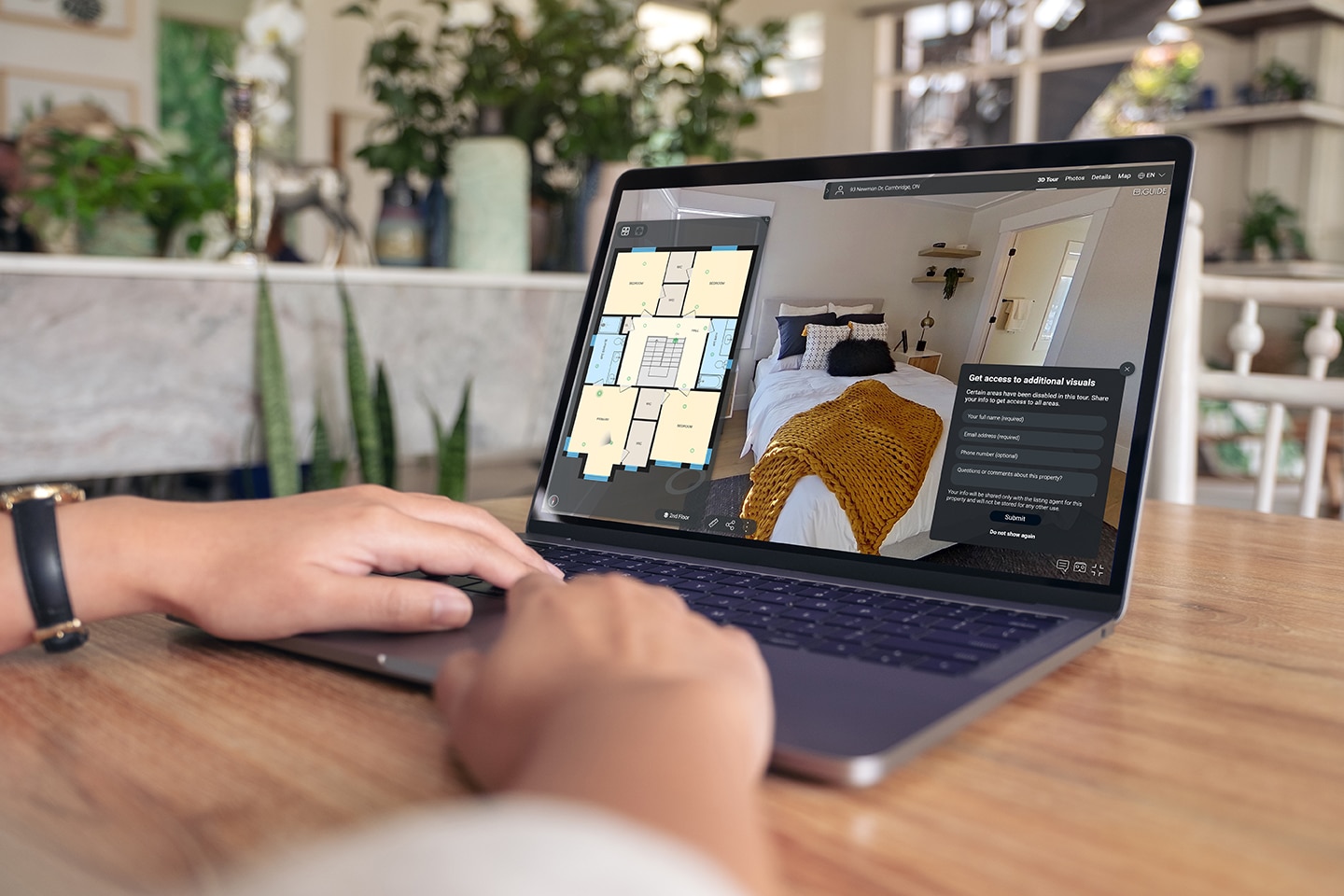 Person using a laptop to explore an iGUIDE 3D virtual tour of a home, featuring a floor plan and a bedroom with a cozy blanket, showcasing immersive real estate technology for enhanced property viewing.