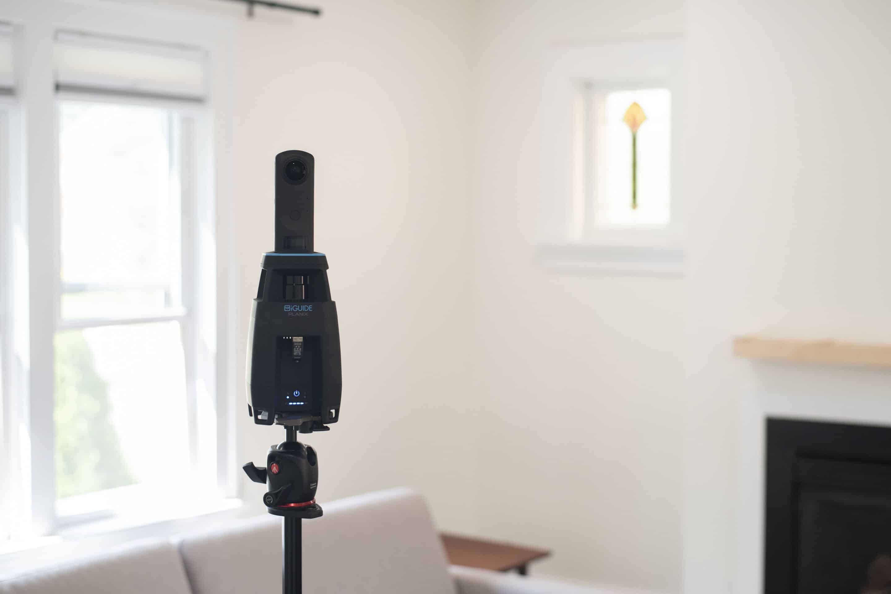 3D camera setup for iGUIDE virtual tours in a bright, modern living space with a window and fireplace, emphasizing immersive real estate experiences.